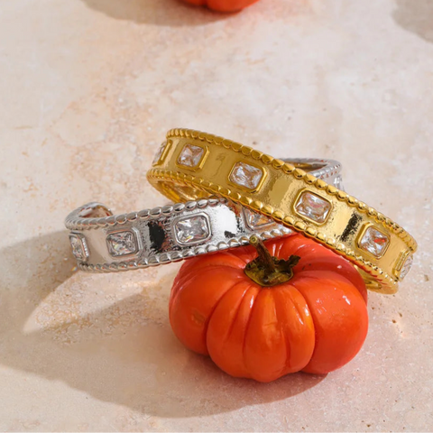 Two rings, one gold and one silver, on a small orange pumpkin with another pumpkin in the background.