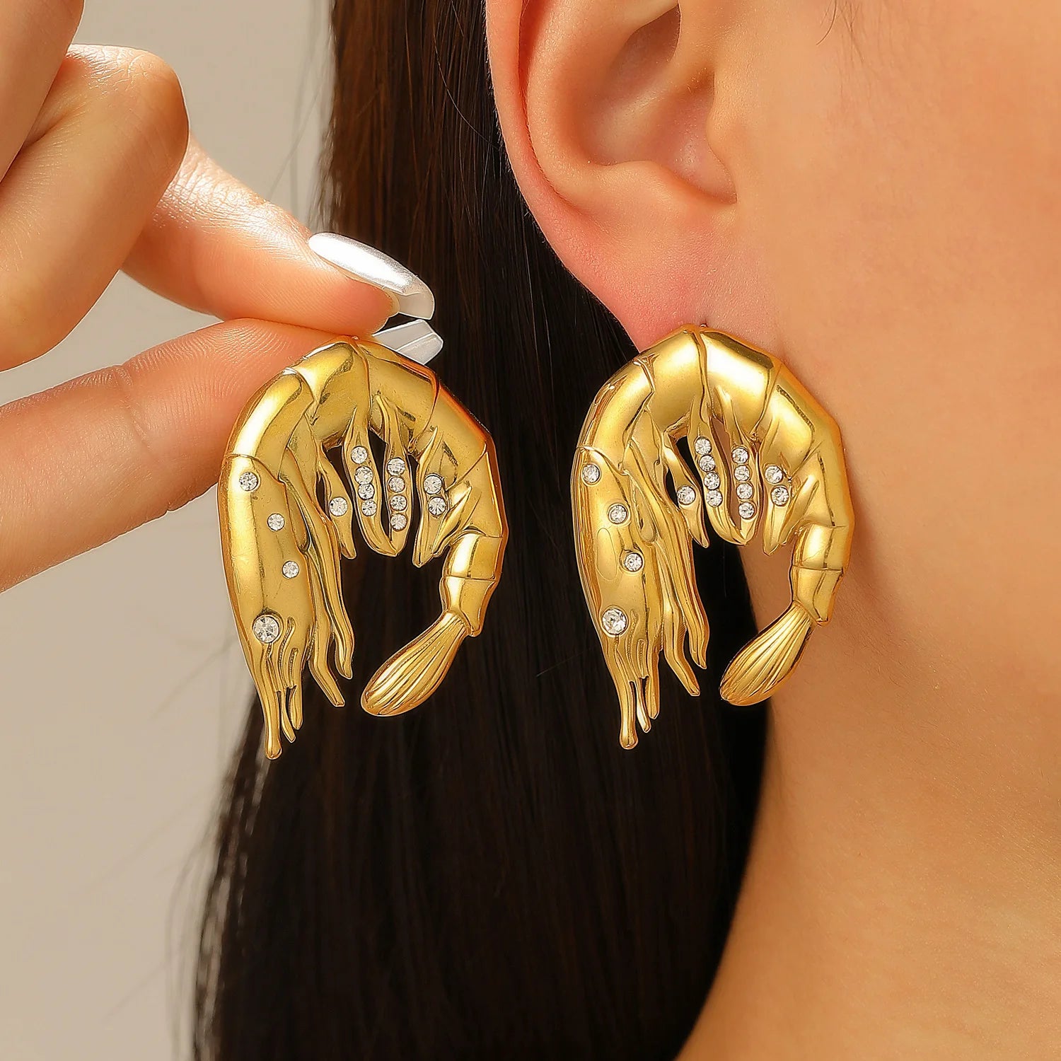 Gold hand-shaped earrings with embedded stones worn by a person.