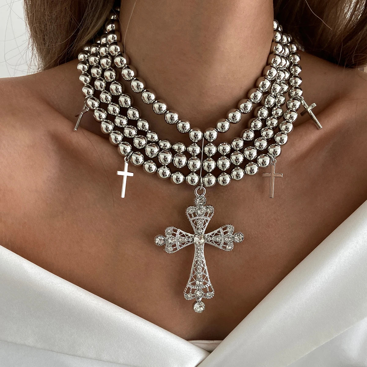 Silver beaded necklace with cross pendants on a person wearing a white garment.